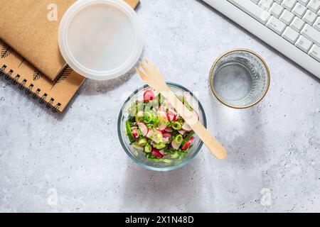 Healthy food in a office. Prepared radish and cucumber salad on  a desk with office supplies Stock Photo
