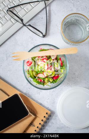 Healthy food in a office. Prepared radish and cucumber salad on  a desk with office supplies Stock Photo