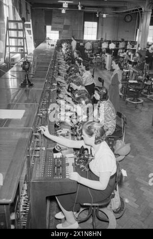 In January 1942, London telephone exchange operators manage TOL calls at an auto-manual switchboard, with trainees observing from the rear. Stock Photo
