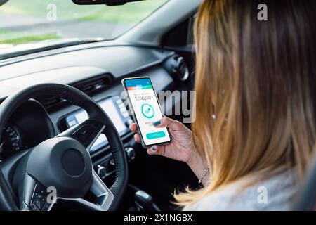 Woman making a digital money transfer with her mobile phone in her car. Stock Photo