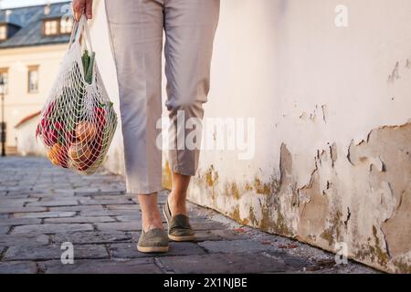 Woman walks on street with reusable mesh bag after shopping food. Zero waste and sustainable plastic free lifestyle Stock Photo