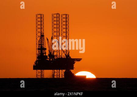 Southport, Merseyside, 04/17/2024  A beautiful sunset nestles into the horizon behind the impressive 'Rowan Norway' jack-up oil rig marine vessel located in the Liverpool Bay off the Irish Sea. This “jack-up” rig has legs 173 metres long that can be deployed to 150 metres and can drill to a depth of 10,670 metres.  The wells will be converted so that they can be reused to store carbon dioxide in the depleted oil and gas reservoirs beneath the seabed as part of a wider HyNet Carbon Capture and Storage project.  Credit: Cernan Elias/Alamy Live News Stock Photo