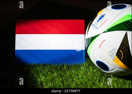 HAMBURG, GERMANY, APRIL 17, 2024: Netherlands national flag and official soccer ball of Euro 2024 football tournament in Germany placed on green grass Stock Photo