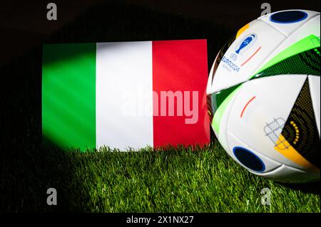 HAMBURG, GERMANY, APRIL 17, 2024: Italy national flag and official soccer ball of Euro 2024 football tournament in Germany placed on green grass. Blac Stock Photo