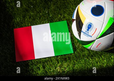 BERLIN, GERMANY, APRIL 17, 2024: Italy national flag and official soccer ball of Euro 2024 football tournament in Germany placed on green grass. Black Stock Photo