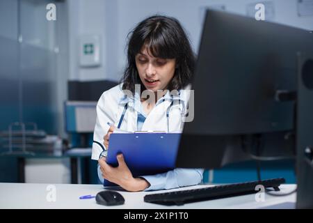 Close-up shot of female practitioner writing medical notes on her clipboard. Detailed image of a caucasian doctor dedicatedly reviewing information from patient consultations. Stock Photo