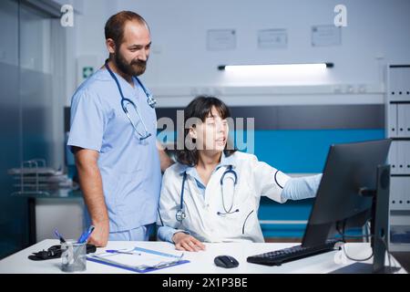Doctor and nurse in clinic office preparing for medical consultations with patients. Their lab coats denote their profession, and the blue scrubs indicate a surgical role. Stock Photo