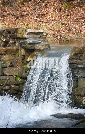 Water pours over the stone wall of the Historic Bush Mill Dam spillway.  Stone wall is made of hand cut stones. Stock Photo