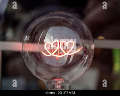 Light bulb with heart-shaped filament on blurry background. Love or Valentine's day concept. Stock Photo