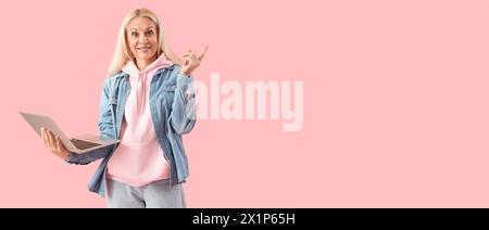 Mature female programmer with laptop showing something on pink background with space for text Stock Photo