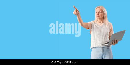 Mature female programmer working with laptop showing something on blue background with space for text Stock Photo