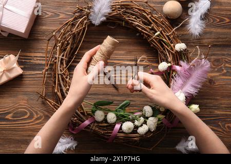 Woman making Easter wreath with eggs, feathers and flowers on brown wooden background Stock Photo