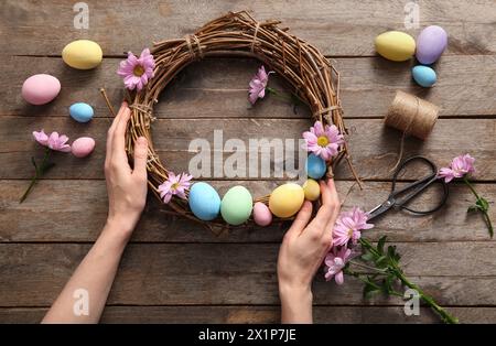 Woman making Easter wreath with painted eggs and flowers on brown wooden background Stock Photo