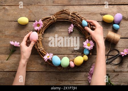Woman making Easter wreath with painted eggs and flowers on brown wooden background Stock Photo