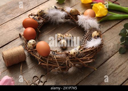 Tulips, supplies for creating Easter wreath with eggs and feathers on brown wooden background Stock Photo