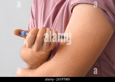 Handsome young diabetic man giving himself insulin injection on grey background, closeup Stock Photo