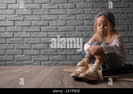 homeless little girl sitting on floor near grey brick wall Stock Photo