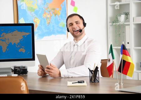 Male travel agent with headset and tablet computer working at table in office Stock Photo