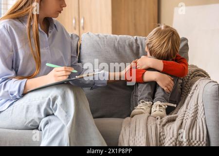 Female psychologist working with stressed little boy on sofa in office. World Autism Awareness Day Stock Photo
