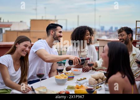 Group of laughing diverse friends for meal party on rooftop terrace together Stock Photo