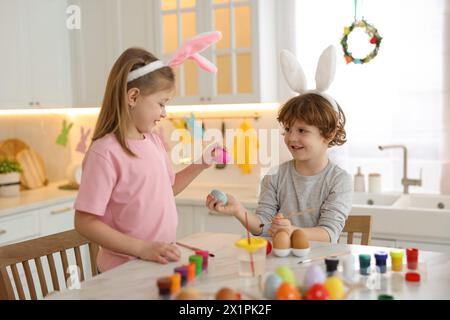 Easter celebration. Cute children with bunny ears having fun while painting eggs at white marble table in kitchen Stock Photo