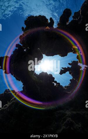 A circular rainbow is created underwater with sun rays through the coral reef hitting the camera dome port Stock Photo