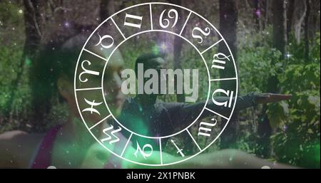 Diverse friends practicing yoga in forest, surrounded by horoscope symbols Stock Photo