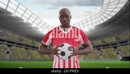 Man in red and white striped jersey holding soccer ball stands in stadium Stock Photo