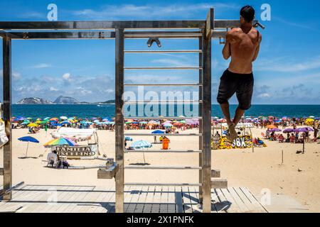 A Young Man Doing Pull Ups At An Exercise Station On Ipanema Beach, Ipanema, Rio de Janeiro, Brasil. Stock Photo
