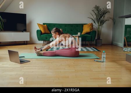 Sporty woman doing stretching exercises on a yoga mat in a living room Stock Photo