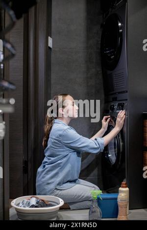 Woman turn on automatic washing machine or select program with knob on control panel in bathroom, modern appliances at home Stock Photo
