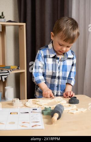Two-year-old boy making his first cookie with a recipe book for toddlers. Stock Photo