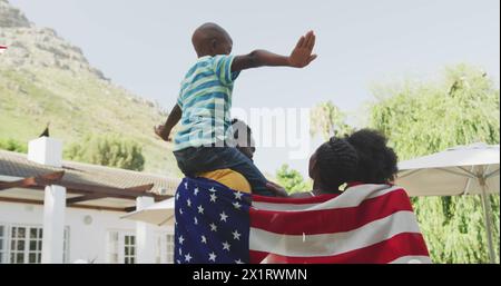 Black young man lifts child on shoulders, both in casual wear Stock Photo