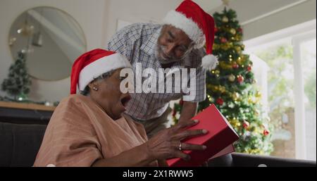 Senior biracial couple celebrating Christmas, grandmother opening gift Stock Photo