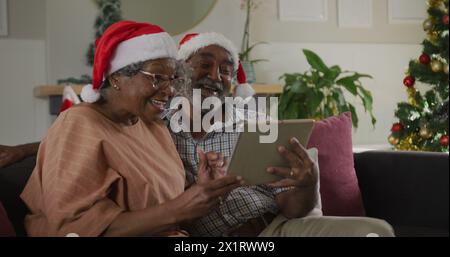 Senior biracial couple wearing Santa hats looking at tablet Stock Photo