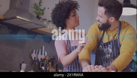 Diverse couple, wearing aprons, standing in kitchen Stock Photo