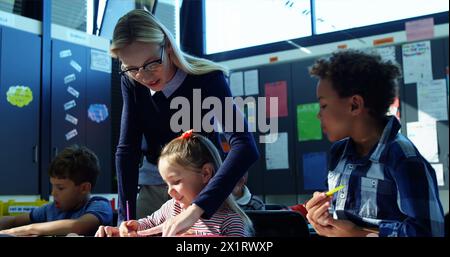 In school, young Caucasian female teacher is helping a diverse group of students Stock Photo