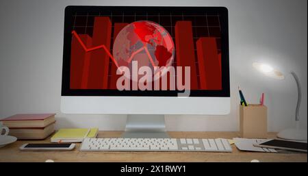 A computer screen displaying red world map and graphs sits on a desk Stock Photo