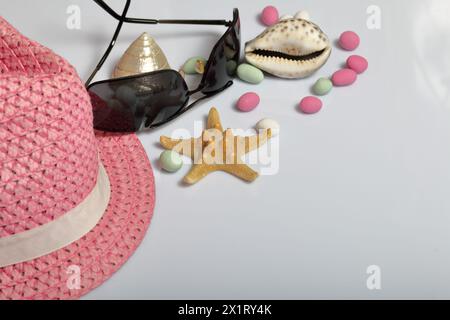 Accessories for summer holidays. Hat and sunglasses on a white background. Near colored pebbles, seashells and starfish. Stock Photo