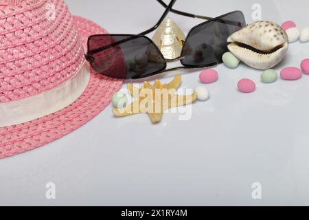 Accessories for summer holidays. Hat and sunglasses on a white background. Near colored pebbles, seashells and starfish. Stock Photo