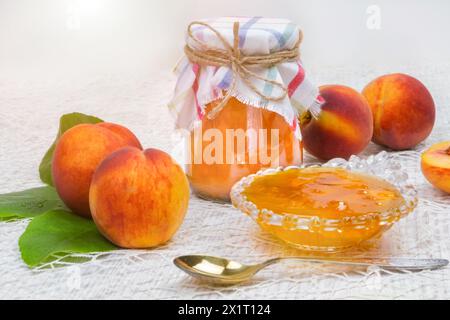 Jam of peaches on the table in a jar, next to a bowl of jam and spoons, peaches Stock Photo