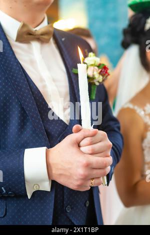 Bride and groom in golden crowns standing with candles in hands during wedding ceremony. Spiritual couple. Wedding matrimony in church. Emotional roma Stock Photo