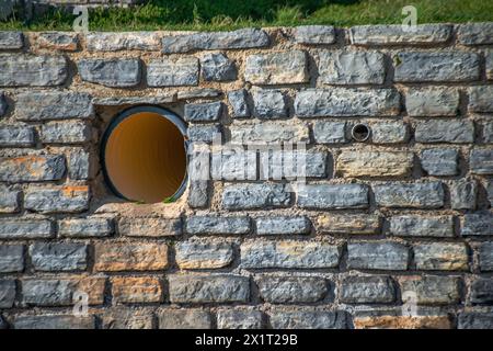 Industrial meets ancient in the juxtaposition of a big pipe against sturdy stone walls, merging modernity with history. Stock Photo