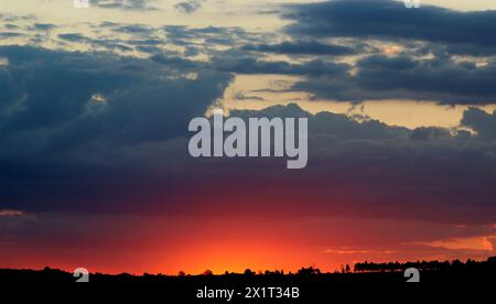 a large landscape photo of a sunset with colours of yellow, orange, pink, purple and going into big grey storm clouds trees Stock Photo