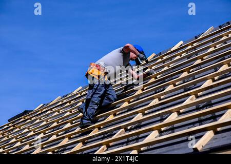 Repair and replacement of the old roof with a new one. Construction worker in protective clothing standing on roof with tools. Stock Photo