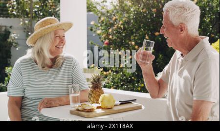 Senior, couple or relax on patio with water for retirement, planning vacation for anniversary. Husband, wife or old in garden for talk with pineapple Stock Photo