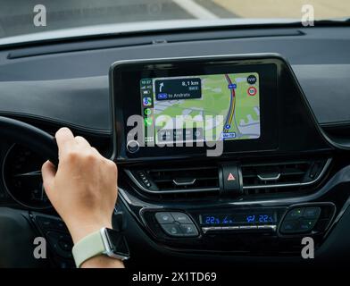 Strasbourg, France - Jun 28, 2023: Driver's hand on wheel with Apple CarPlay displaying route to Andratx on car's dashboard screen in Mallorca, Spain - tech made in Cupertino Stock Photo
