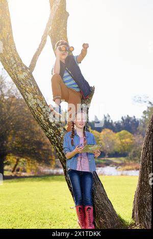 Tree, siblings and search with binoculars, pointing and explore with compass and map. Adventure, navigation and fun hobby for children on vacation Stock Photo