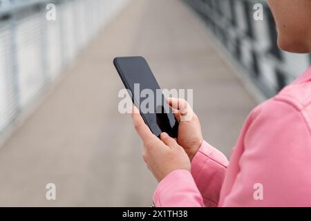 Urban woman wearing pink coloured jacket with black smartphone in her hands. Stock Photo