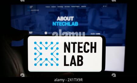 Person holding cellphone with logo of Russian facial recognition company NtechLab (Findface) in front of webpage. Focus on phone display. Stock Photo